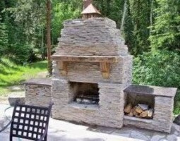 outdoor stone fireplace in front of trees by McMahon Landscape