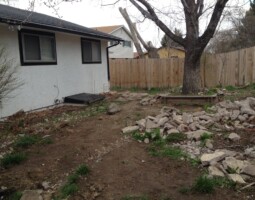 start of landscaping on yard behind white house with black trim and wood fence by McMahon Landscape