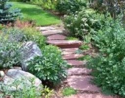 landscape with stone path and green bushes and large rocks by McMahon Landscape